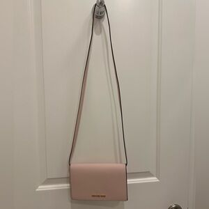 Small Light Pink Michael Kors purse with a strap.